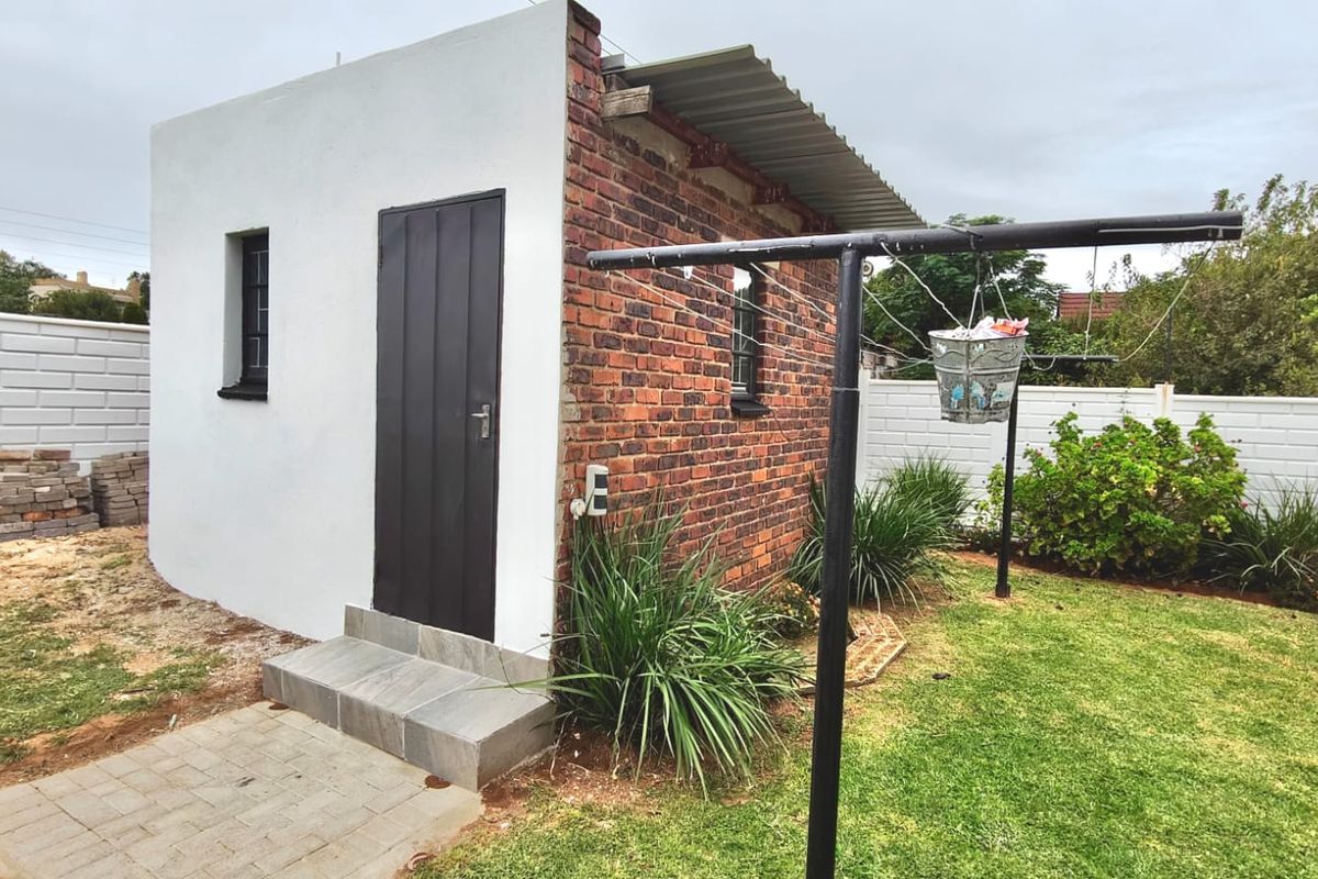 Rear view of a small outbuilding featuring a mix of plastered and exposed brick finishes with a corrugated metal roof and tiled entrance steps.