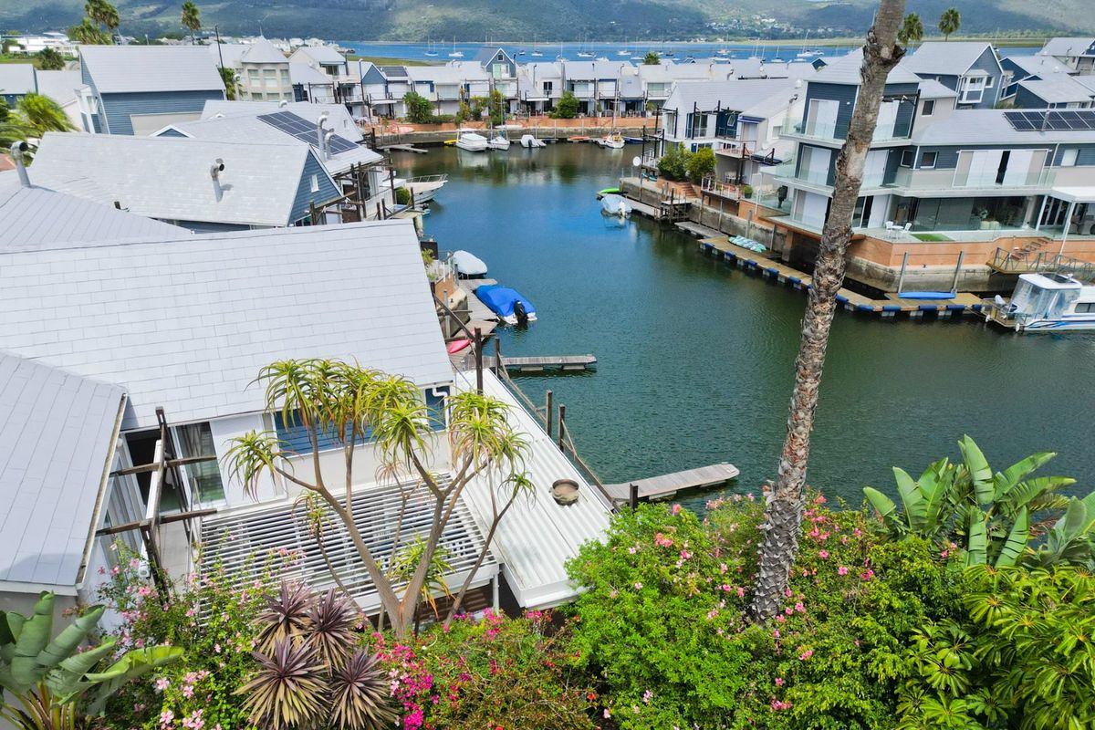 Aerial view of a waterfront residential estate featuring modern homes with metal roofs, solar panels, and private jetty access to the canal.