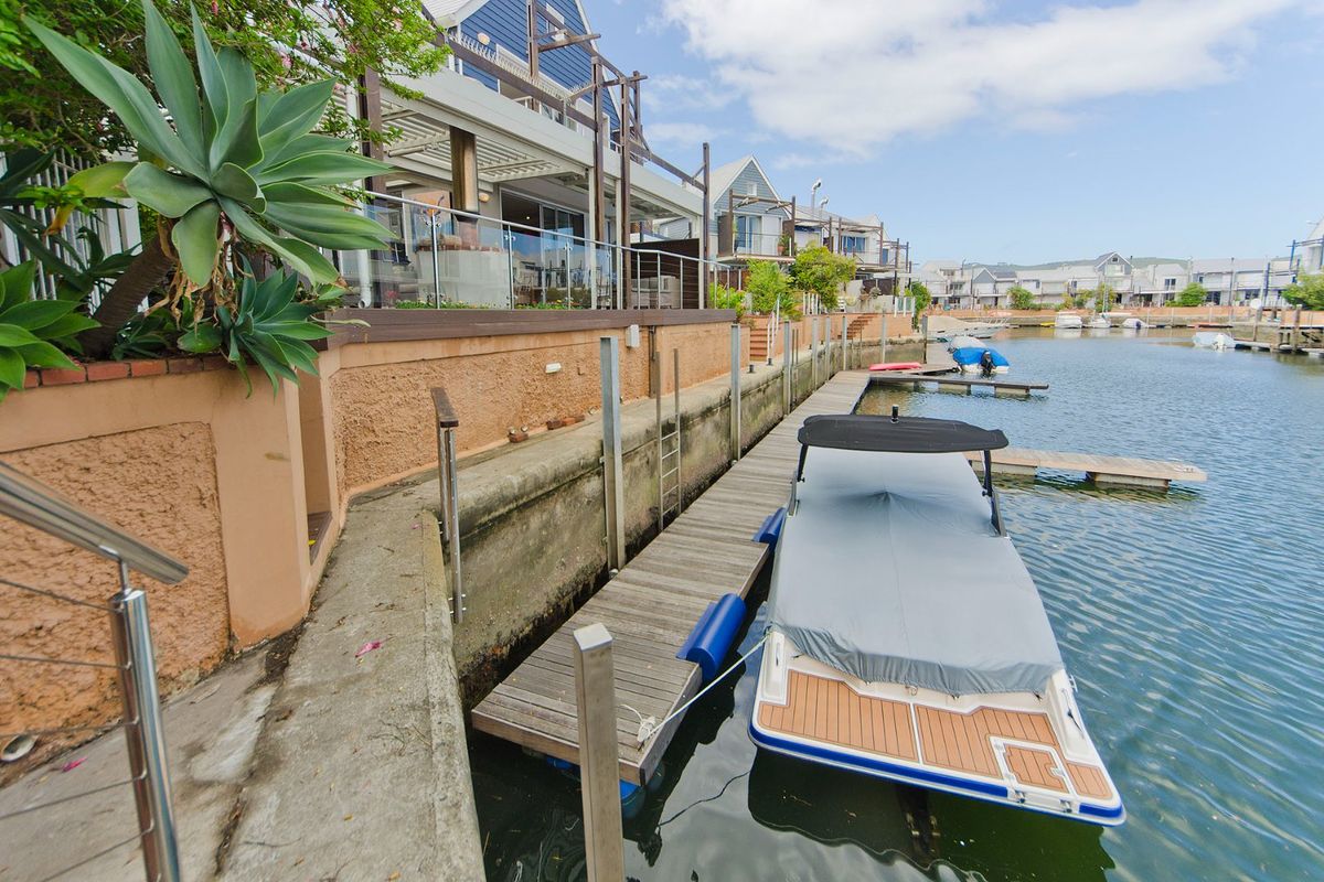 Waterfront view of the rear exterior featuring a private jetty, concrete retaining wall, and direct access to the canal.