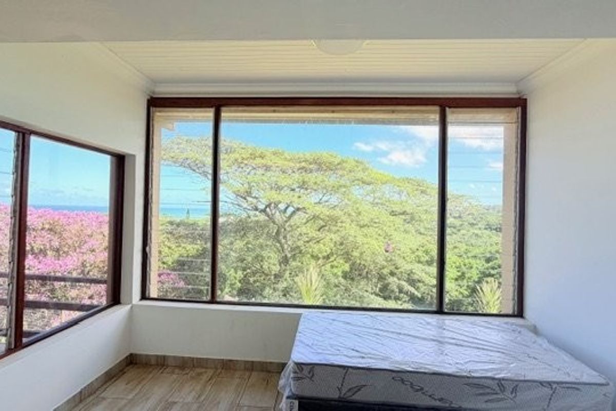 A bright, empty bedroom featuring large picture windows with expansive views, timber frames, and tiled flooring.