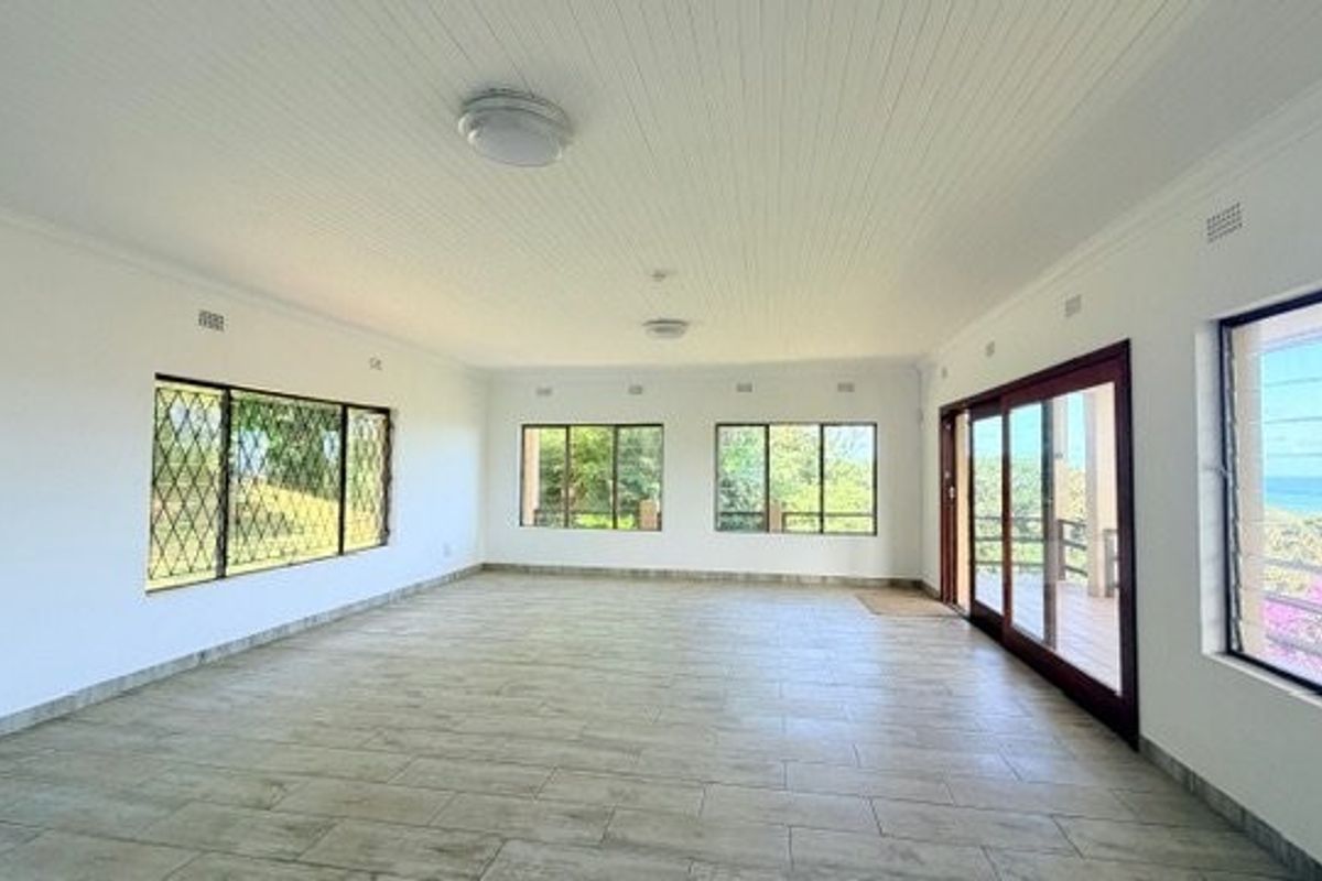 Spacious, light-filled living area featuring tiled floors, tongue and groove ceilings, and large windows with security bars, offering views and access to the outdoors.