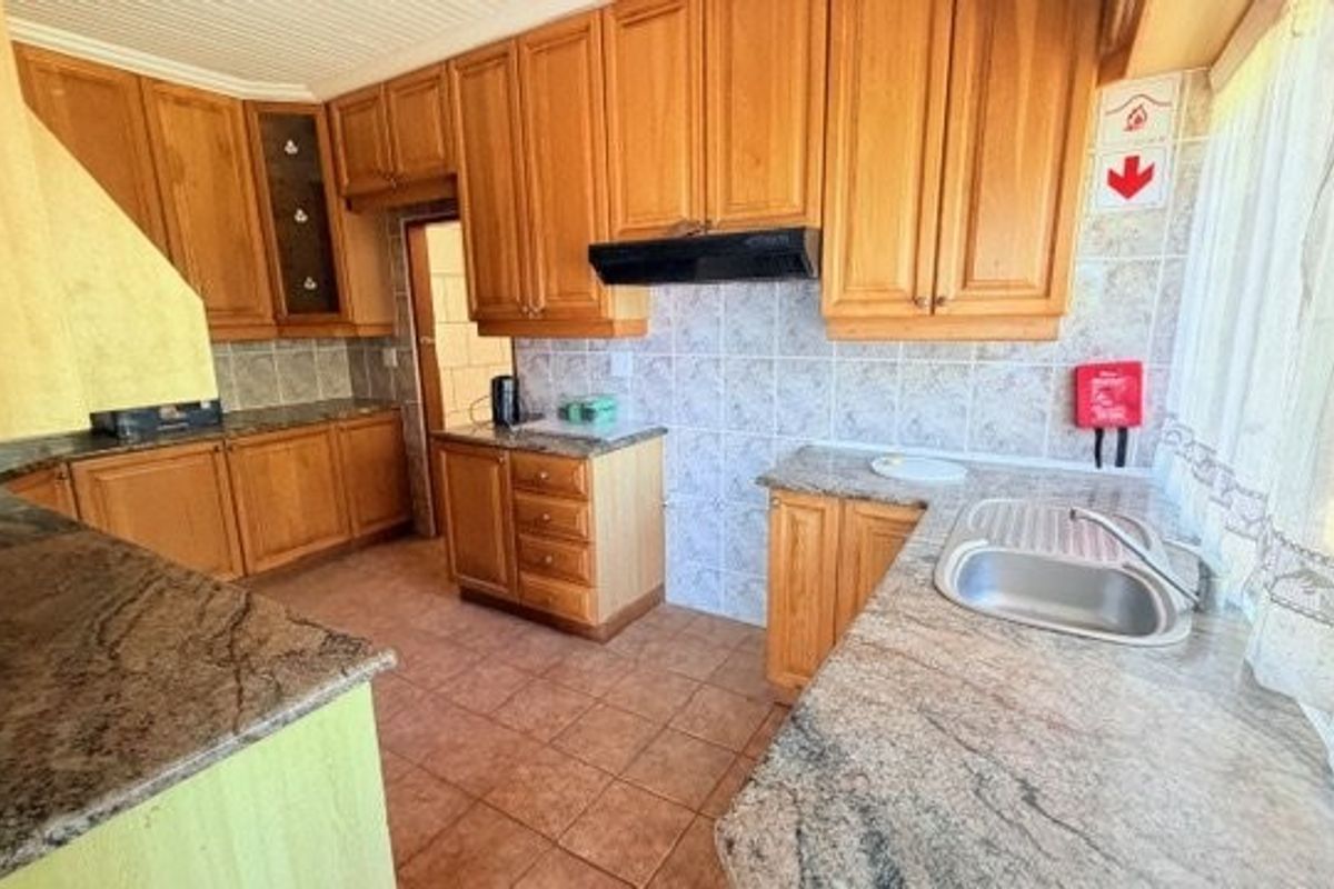 A functional kitchen featuring wooden cabinetry, granite countertops, a stainless steel sink, and tiled finishes, offering a classic layout with ample storage space.