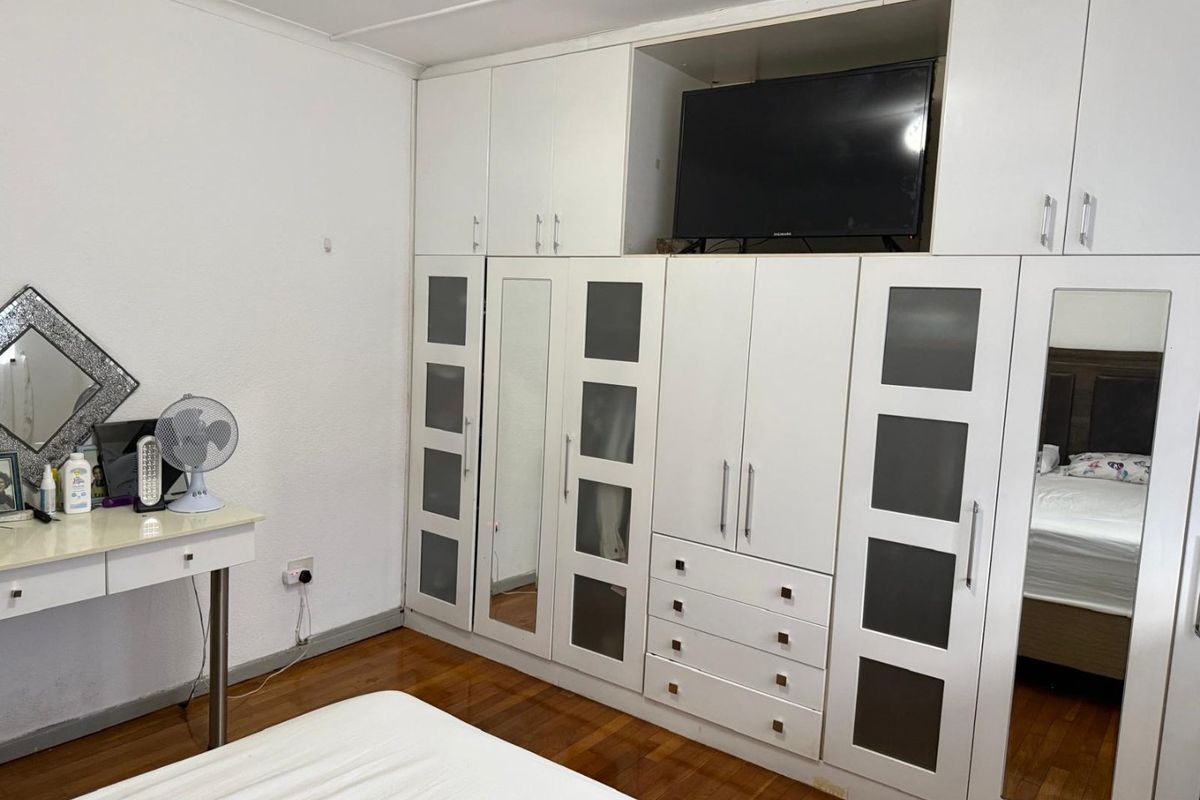 A bedroom featuring extensive built-in white cabinetry with integrated shelving, drawers, and mirrored panels, complemented by polished wooden flooring.