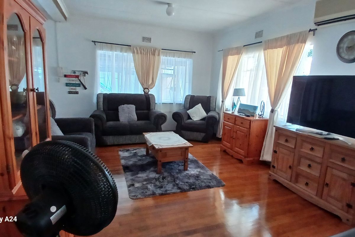 A spacious living room featuring polished wooden flooring, large windows with natural light, and a wall-mounted air conditioning unit.