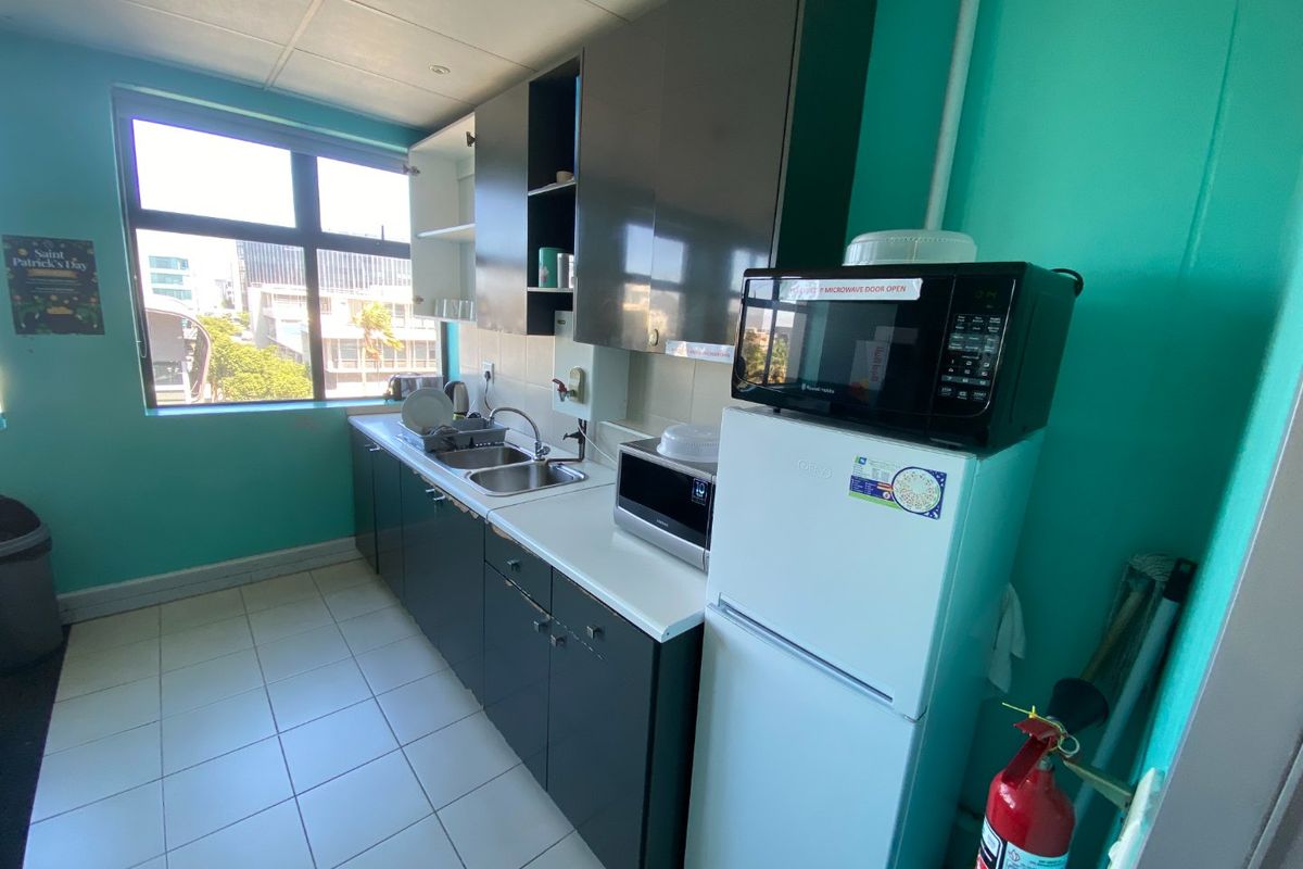A functional commercial kitchenette featuring dark cabinetry, a stainless steel sink, tiled flooring, and a large window providing natural light.