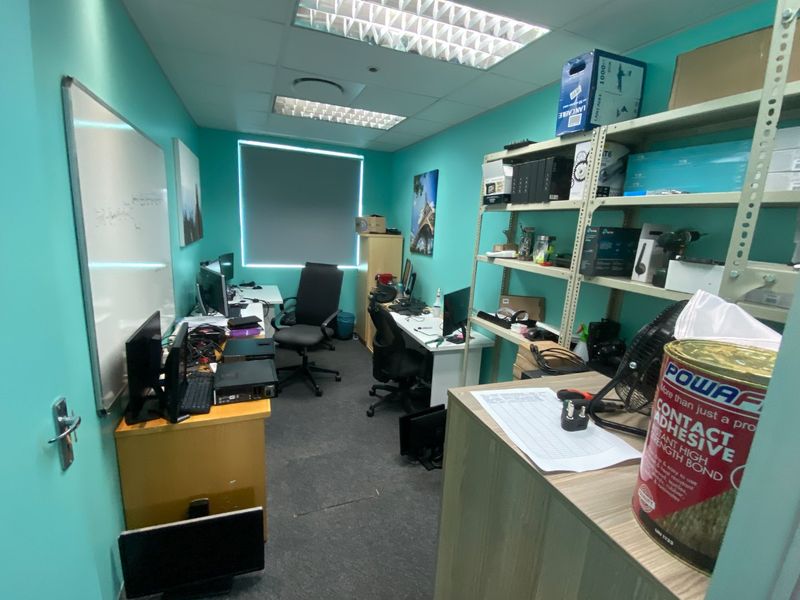 A functional commercial office space featuring a suspended ceiling, recessed lighting, and a wall-mounted whiteboard, suitable for a professional work environment.