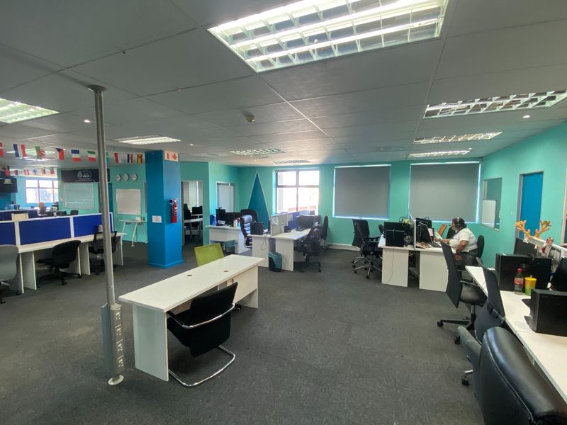 Open-plan commercial office space featuring suspended ceilings, recessed lighting, roller blinds, and carpeted flooring, suitable for a professional work environment.