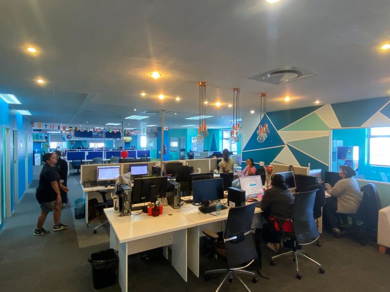 A spacious open-plan commercial office area featuring built-in workstations, modern pendant lighting, recessed ceiling lights, and carpeted flooring.