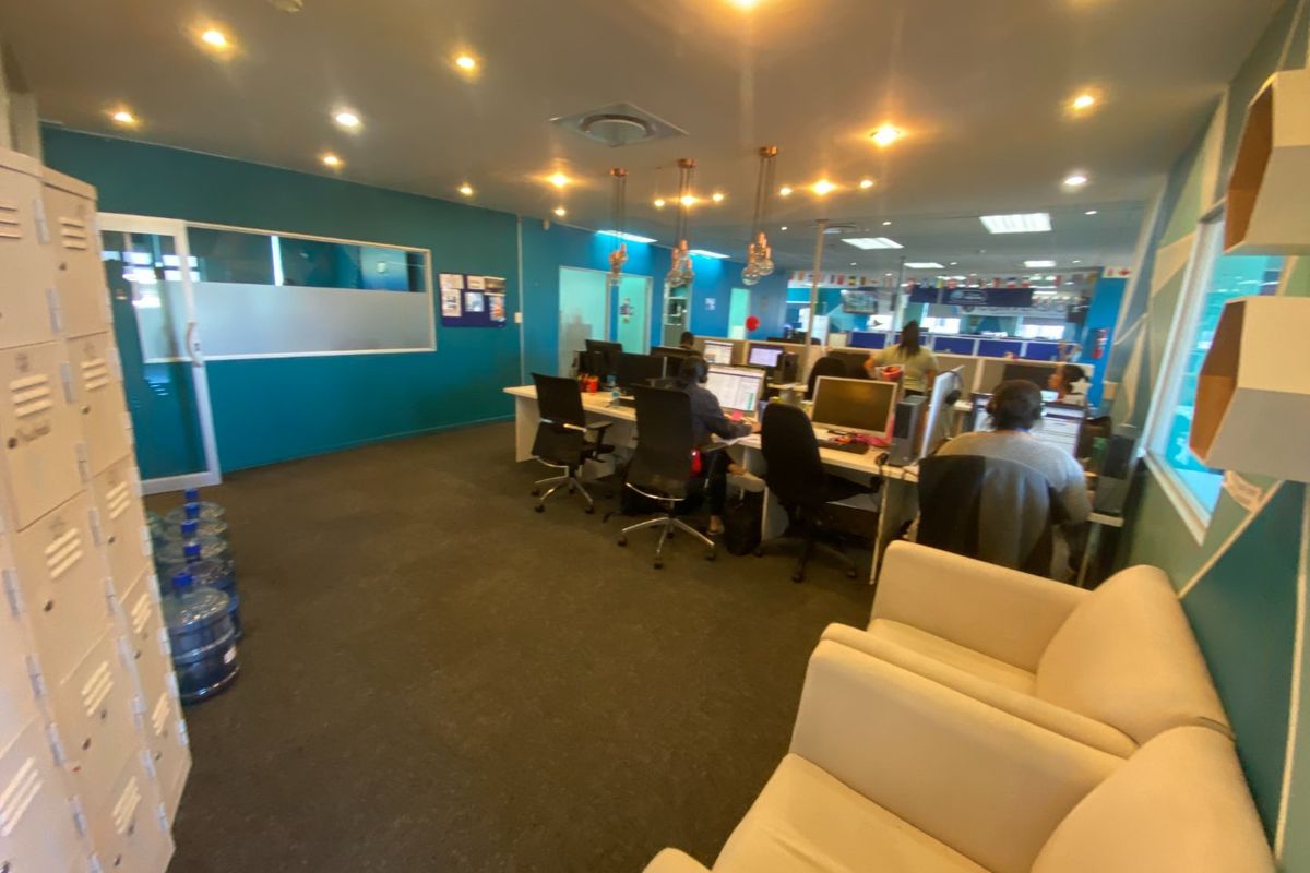 A functional open-plan office space featuring recessed lighting, carpeted flooring, built-in storage lockers, and a glass partition wall.