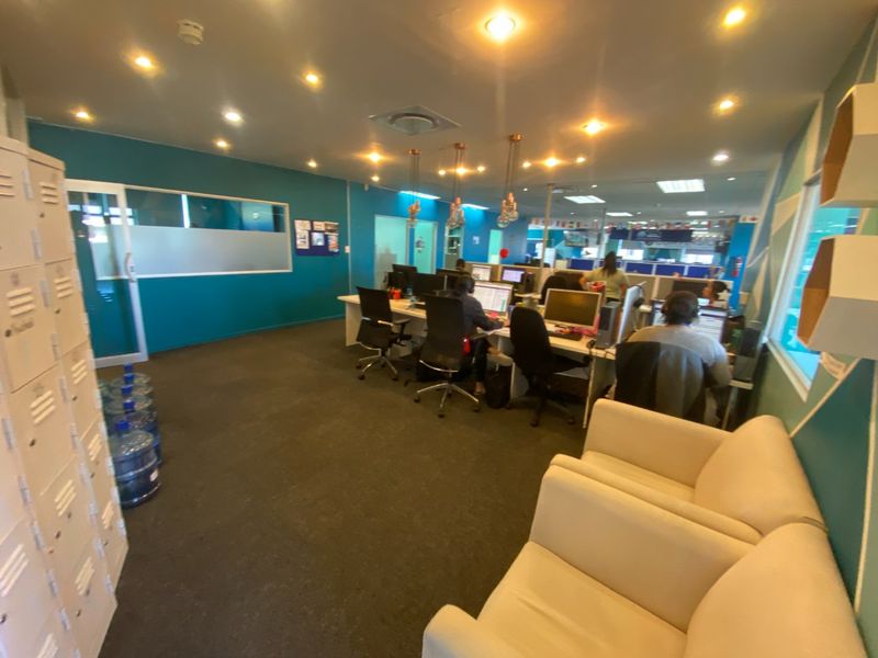 A functional open-plan office space featuring recessed lighting, carpeted flooring, built-in storage lockers, and a glass partition wall.