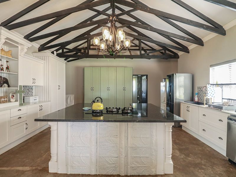 Spacious farmhouse kitchen featuring exposed timber trusses, a large central island with granite countertop, gas hob, and ample built-in cabinetry.