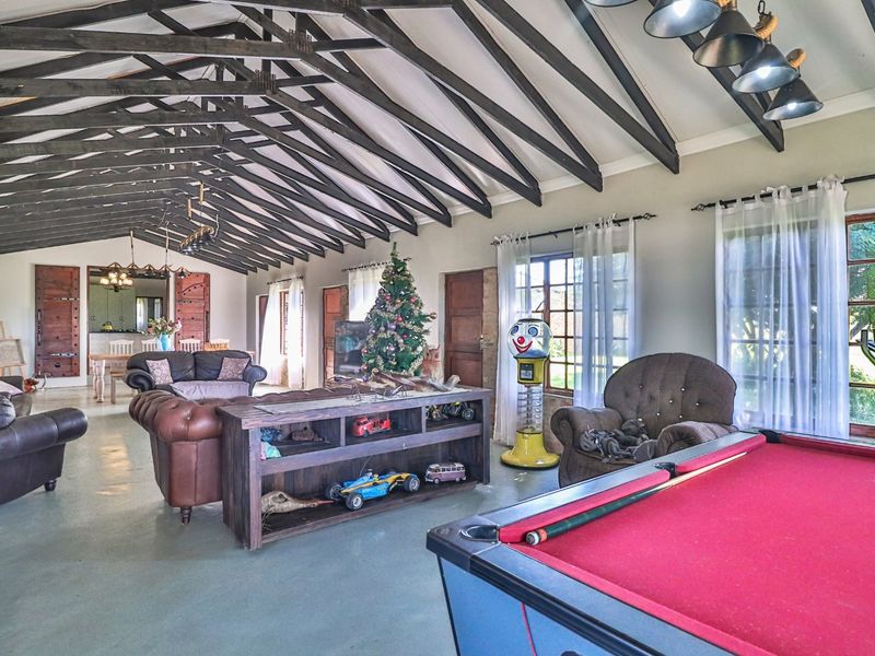 Spacious open-plan living area featuring high vaulted ceilings with exposed timber trusses, concrete flooring, and multiple sets of french doors providing natural light.