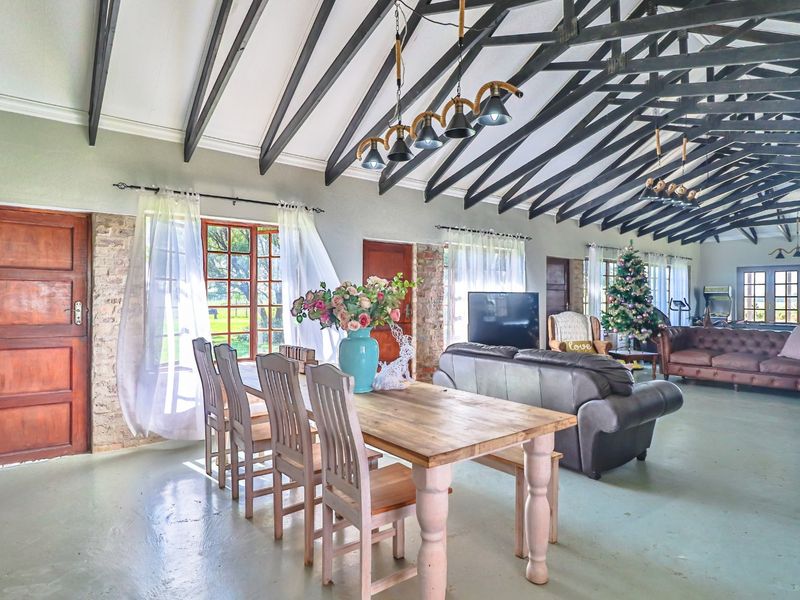 Spacious open-plan living and dining area featuring high vaulted ceilings with exposed timber trusses, polished concrete floors, and large timber-framed windows.