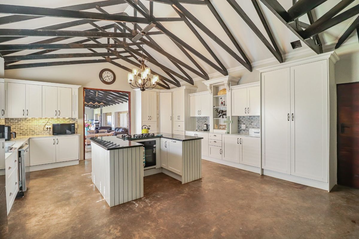 Spacious farmhouse kitchen featuring high vaulted ceilings with exposed timber trusses, a central island with gas hob, and ample built-in cabinetry.