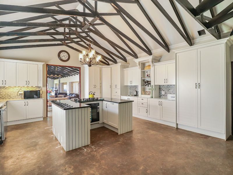 Spacious farmhouse kitchen featuring high vaulted ceilings with exposed timber trusses, a central island with gas hob, and ample built-in cabinetry.