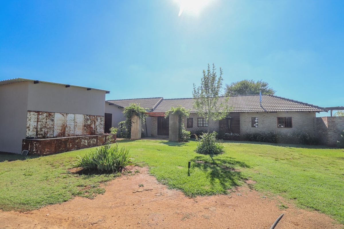 Rear view of a farm-style residence featuring a tiled roof, brick facade, and a spacious garden area with concrete pillars.