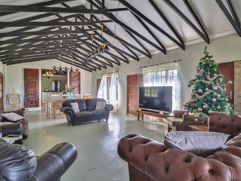 Spacious open-plan living area featuring high vaulted ceilings with exposed timber trusses, painted concrete floors, and rustic exposed brick accents.
