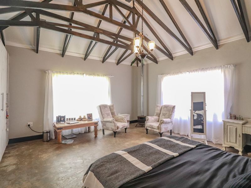 Spacious bedroom featuring a high vaulted ceiling with exposed timber trusses, polished concrete floors, built-in storage, and a cozy wood-burning fireplace.