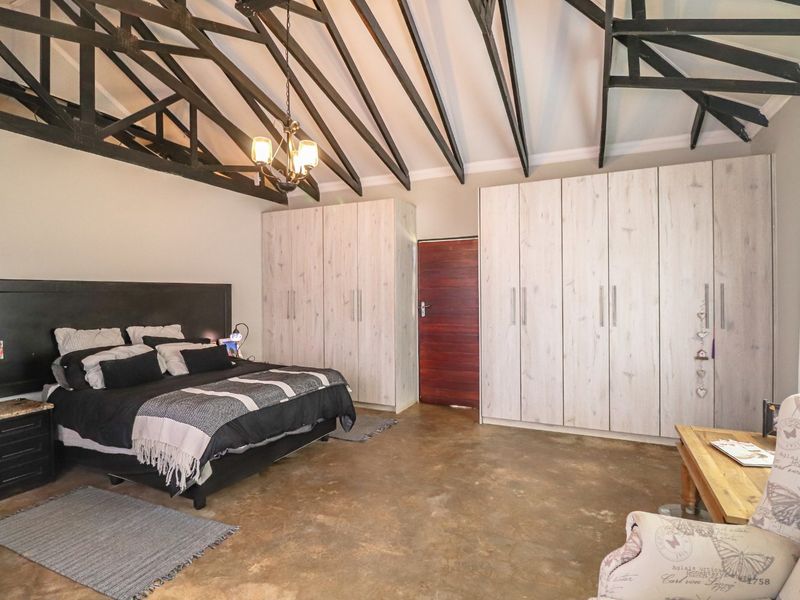 Spacious bedroom featuring exposed timber roof trusses, polished concrete flooring, and extensive built-in cupboard storage.