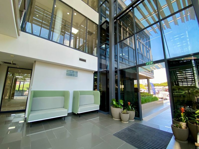 Modern commercial building entrance lobby featuring high ceilings, extensive glass curtain walling, and polished tiled flooring, providing a bright and professional reception area.