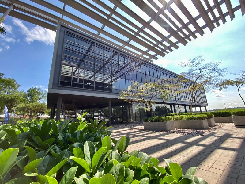 Modern commercial building featuring extensive glass curtain walling, a prominent louvred roof canopy, and a landscaped paved terrace area.