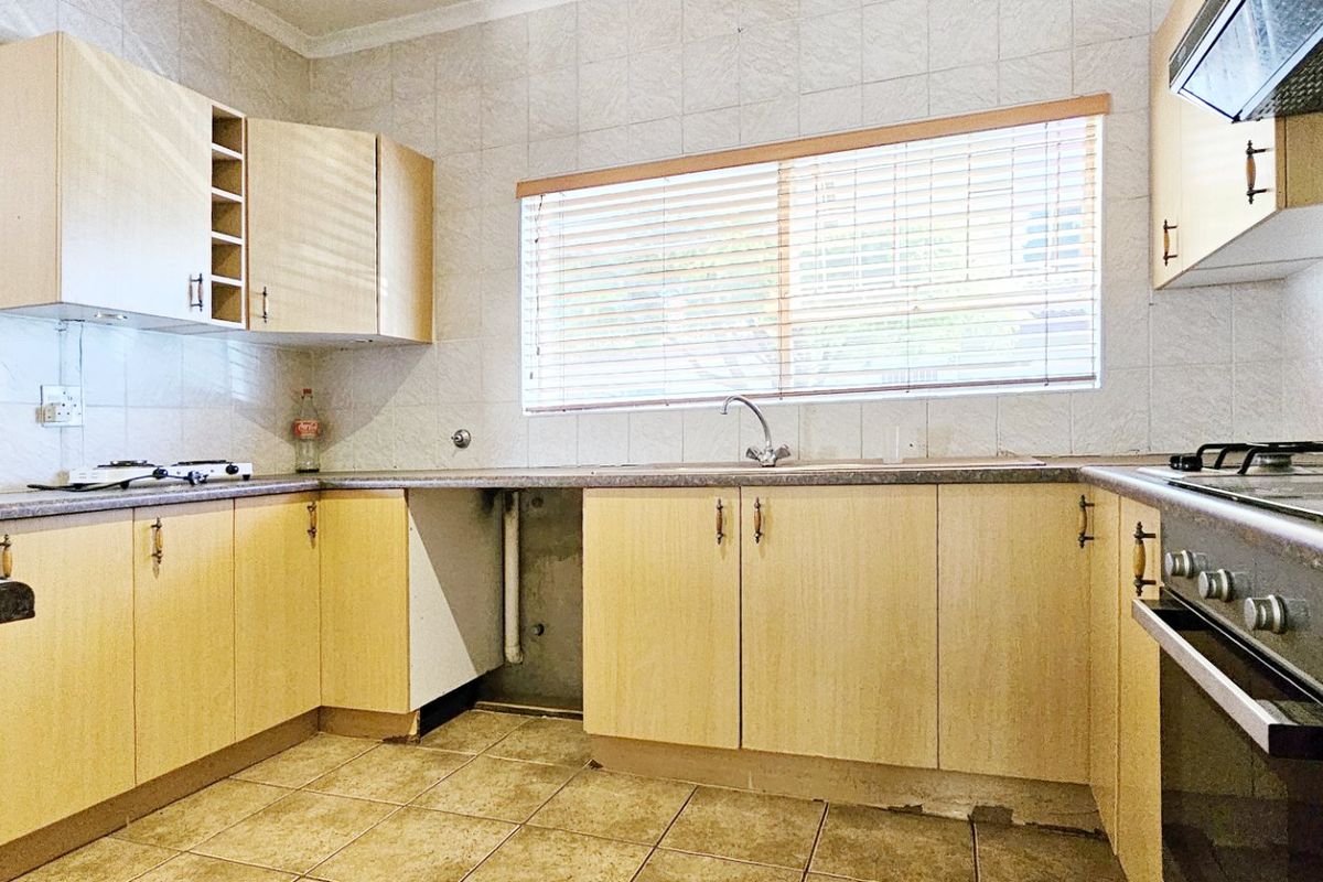 A functional kitchen featuring light wood-tone cabinetry, laminate countertops, a built-in oven with gas hob, and tiled flooring throughout.