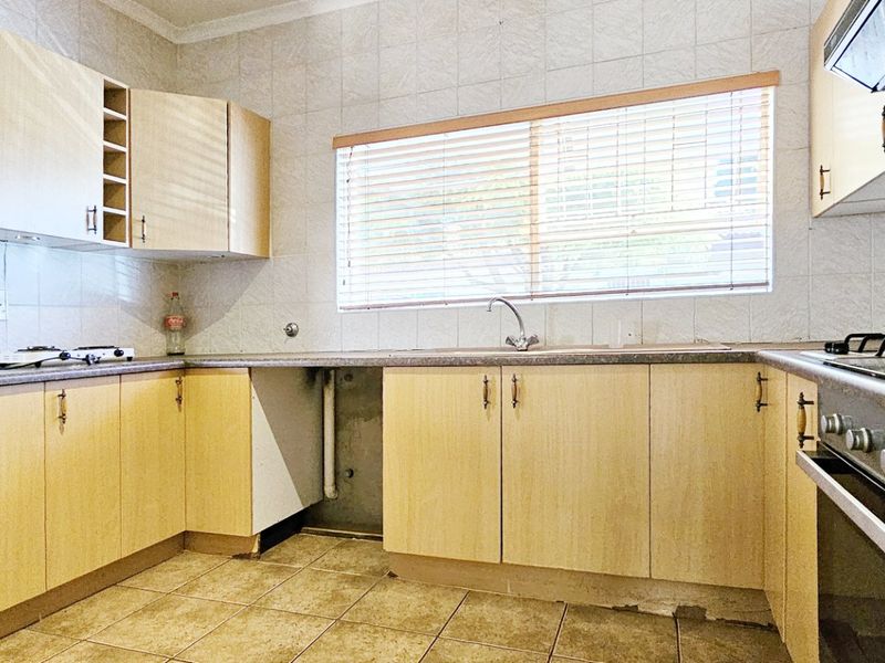 A functional kitchen featuring light wood-tone cabinetry, laminate countertops, a built-in oven with gas hob, and tiled flooring throughout.