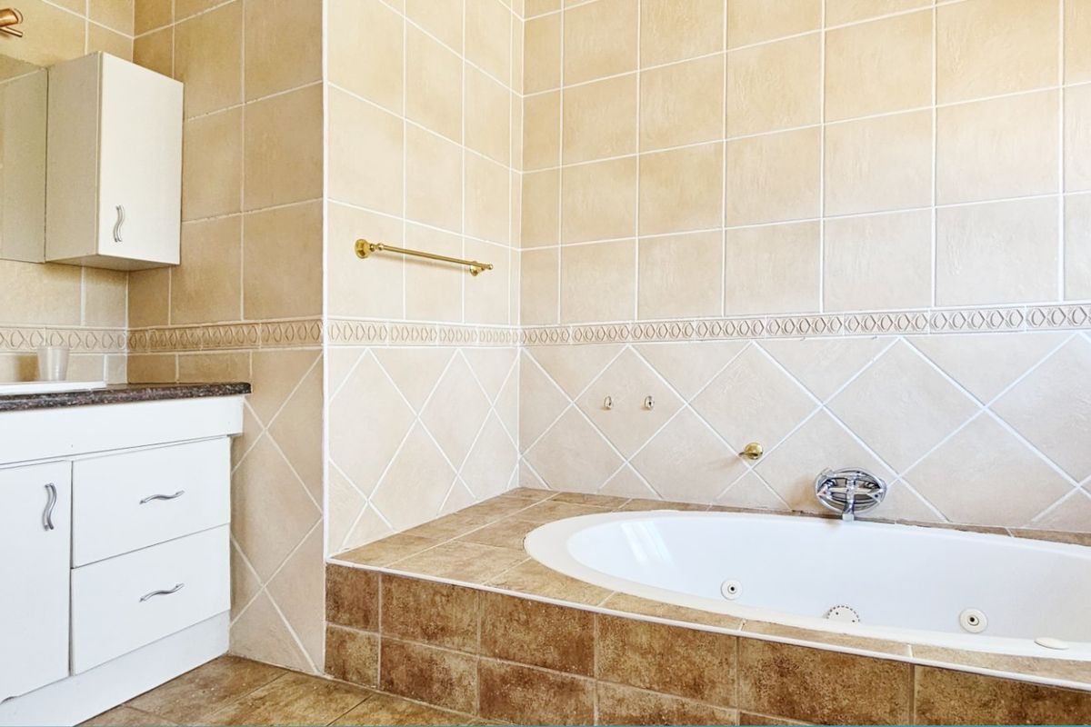 A bathroom featuring a built-in vanity with basin and a tiled drop-in bathtub with neutral wall and floor tiling.