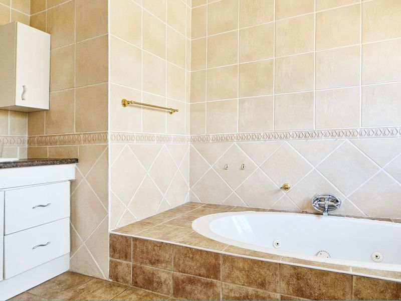 A bathroom featuring a built-in vanity with basin and a tiled drop-in bathtub with neutral wall and floor tiling.