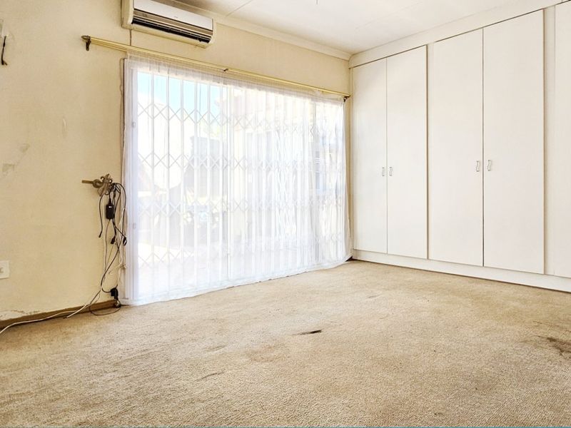 An empty bedroom featuring built-in cupboards, a split-system air conditioner, and a sliding door with security gate, requiring cosmetic updates and flooring replacement.