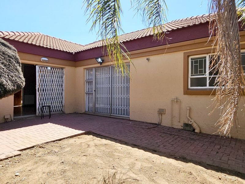 Rear exterior view featuring a paved patio area, a thatch lapa, and secure access points to the main dwelling.