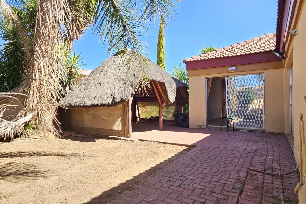 Rear exterior view featuring a paved patio area, a traditional thatch lapa, and access to the home via a sliding door with security gate.
