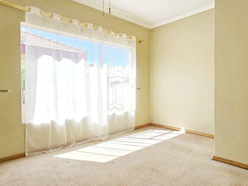 A vacant bedroom featuring neutral wall tones, carpeted flooring, and a large window allowing for natural light.