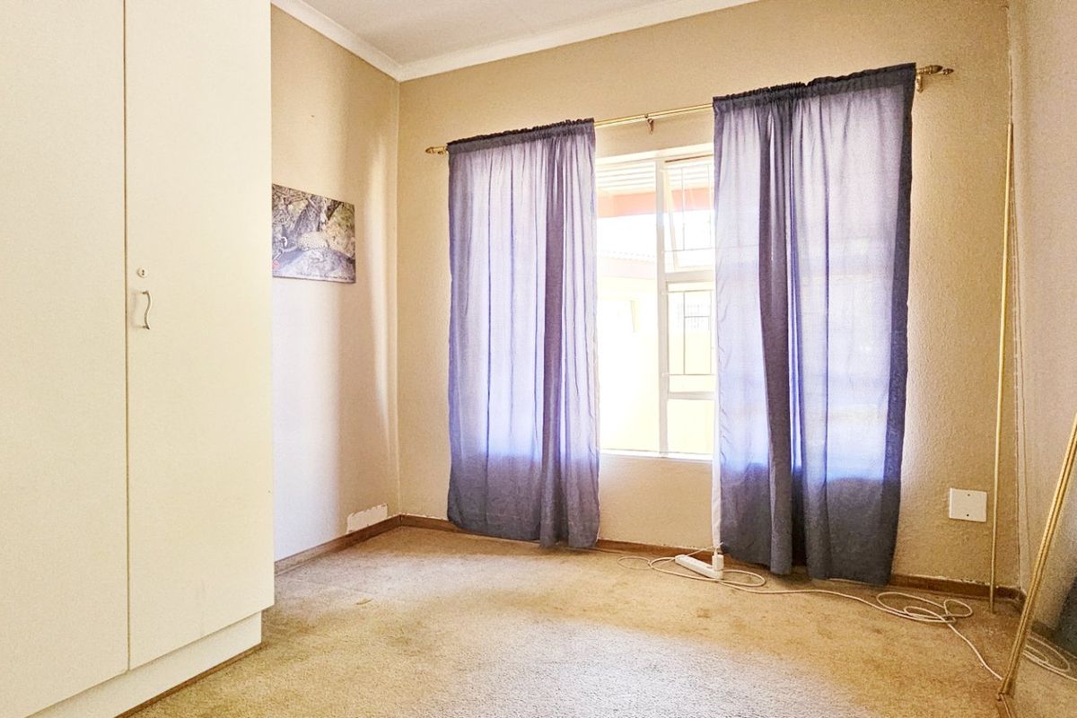 A vacant bedroom featuring built-in cupboards, carpeted flooring, and natural light through a window.