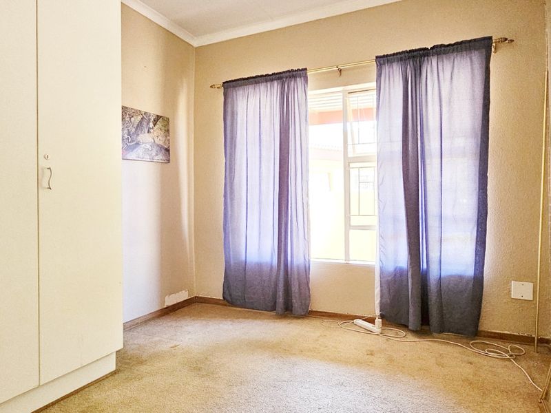 A vacant bedroom featuring built-in cupboards, carpeted flooring, and natural light through a window.