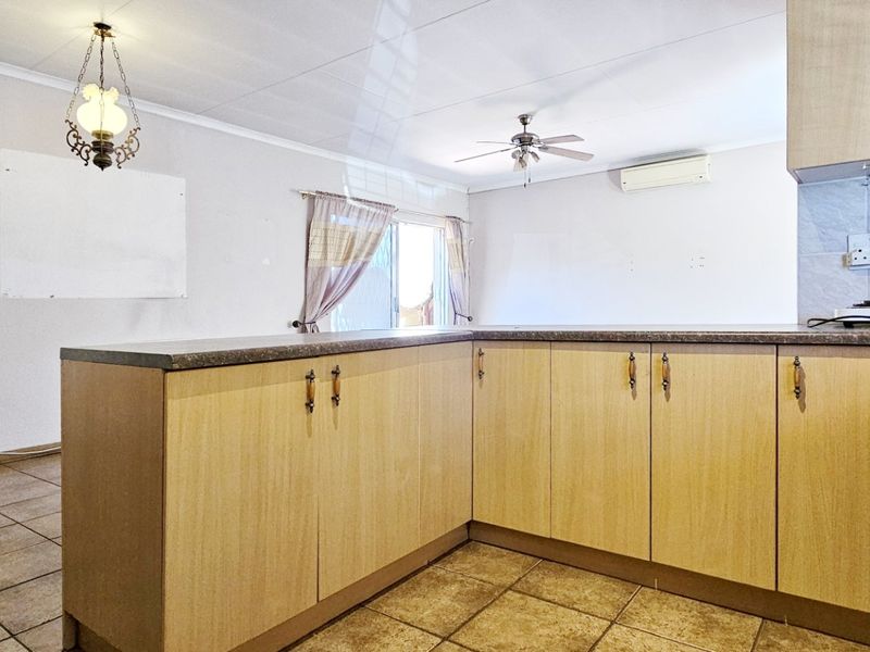 Open plan kitchen and living area featuring tiled flooring, laminate cabinetry, a ceiling fan, and a wall-mounted air conditioning unit.