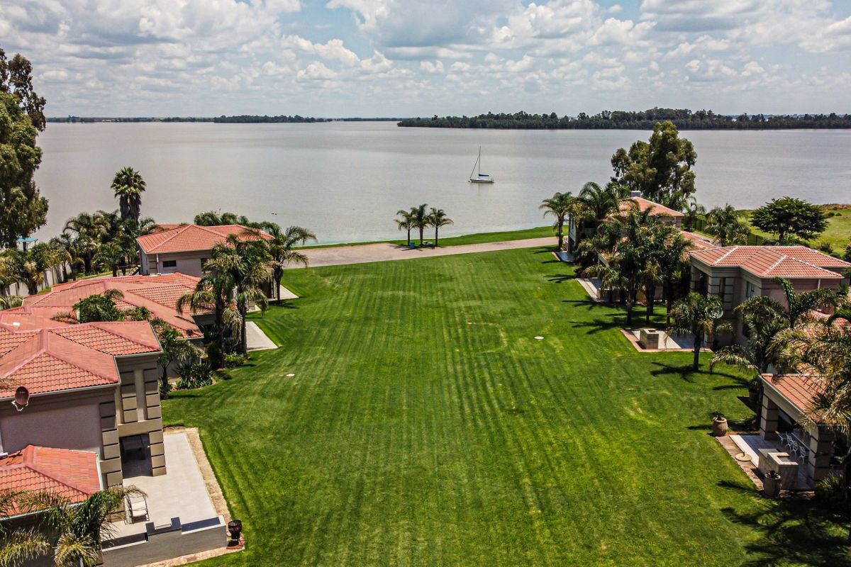 Aerial view of a residential estate featuring multiple units with terracotta roofs, expansive manicured lawns, and direct access to the waterfront.