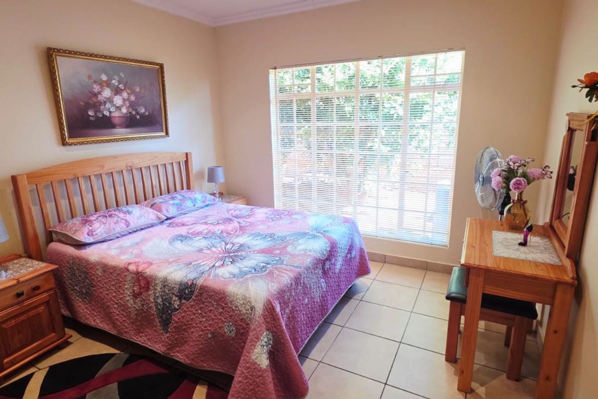 A well-lit bedroom featuring tiled flooring and a large window with fitted blinds, providing natural light and a view of the garden.