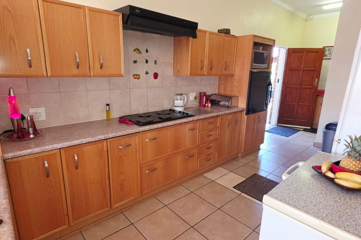 A functional kitchen featuring light wood cabinetry, tiled flooring, a built-in oven, and a gas hob with an extractor fan.