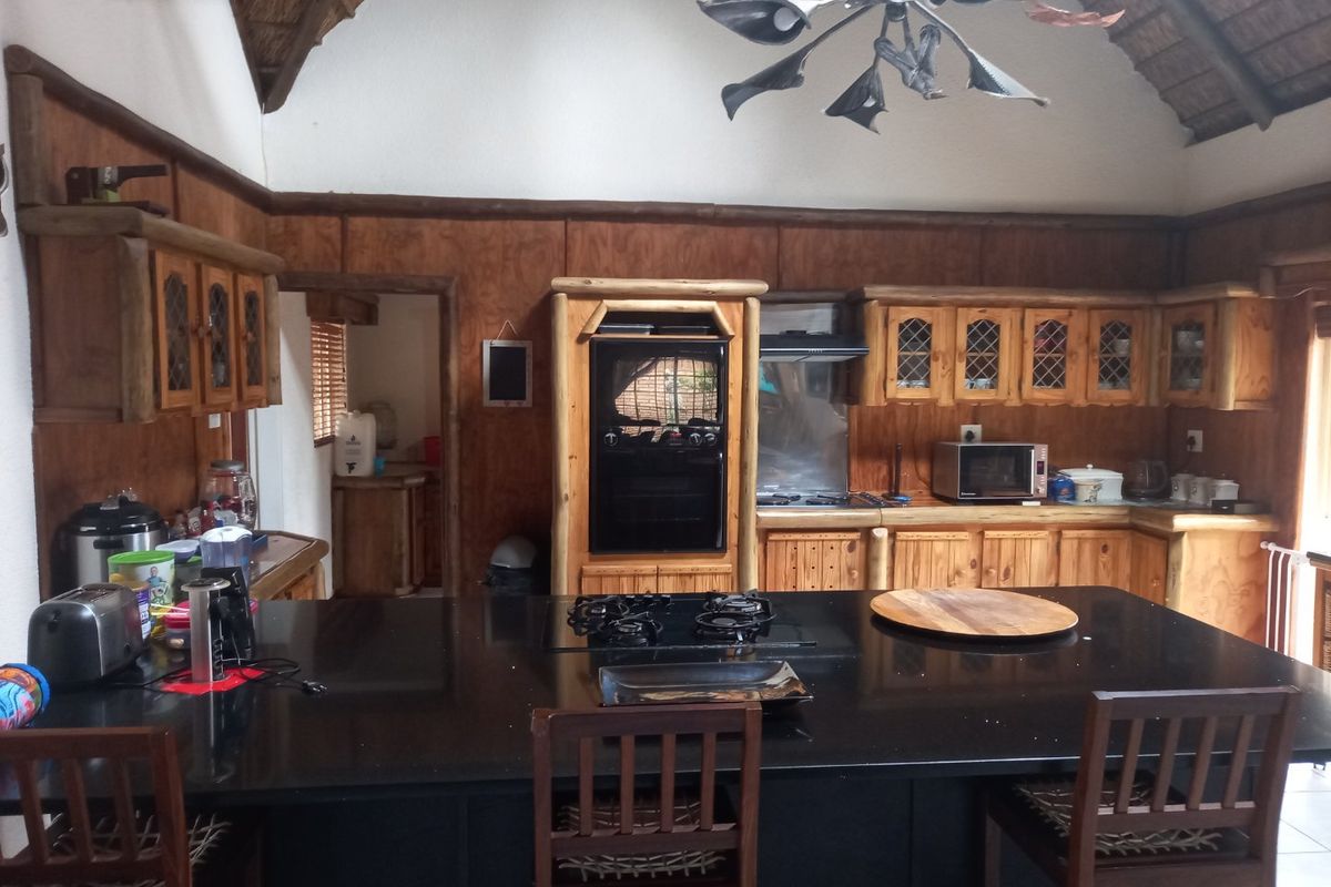 Rustic kitchen featuring timber cabinetry, a large granite island with a built-in gas hob, and a high vaulted thatch ceiling.