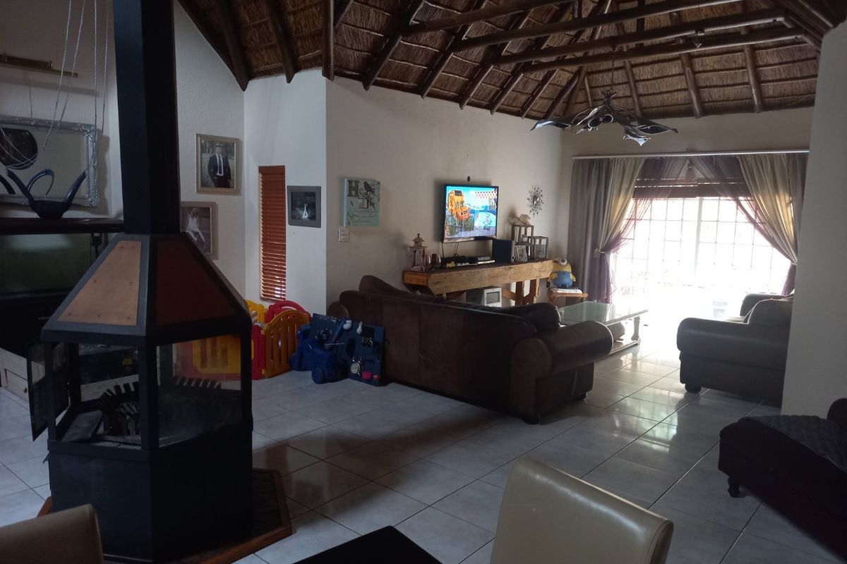 Spacious living area featuring a unique freestanding fireplace, high vaulted thatched ceiling with exposed timber rafters, and large sliding doors leading to the exterior.