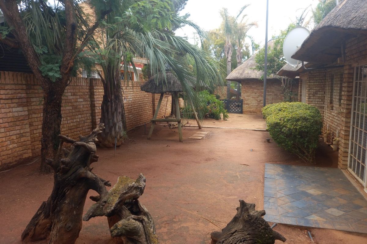 A rear garden area featuring a brick boundary wall, thatched roof structures, and a small tiled patio section.
