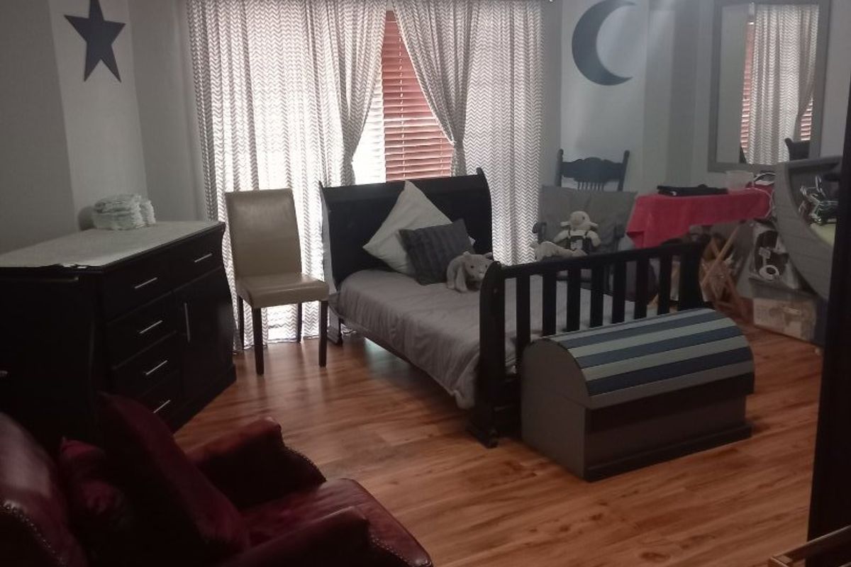 A spacious bedroom featuring laminate flooring, crown molding, and a central ceiling light fixture, offering a comfortable and functional living space.