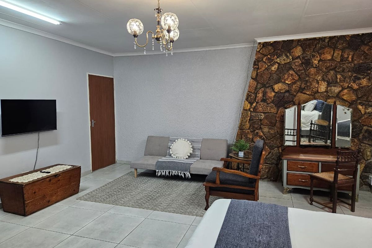 Spacious bedroom featuring a distinctive stone accent wall, neutral tiled flooring, and a classic chandelier fixture.