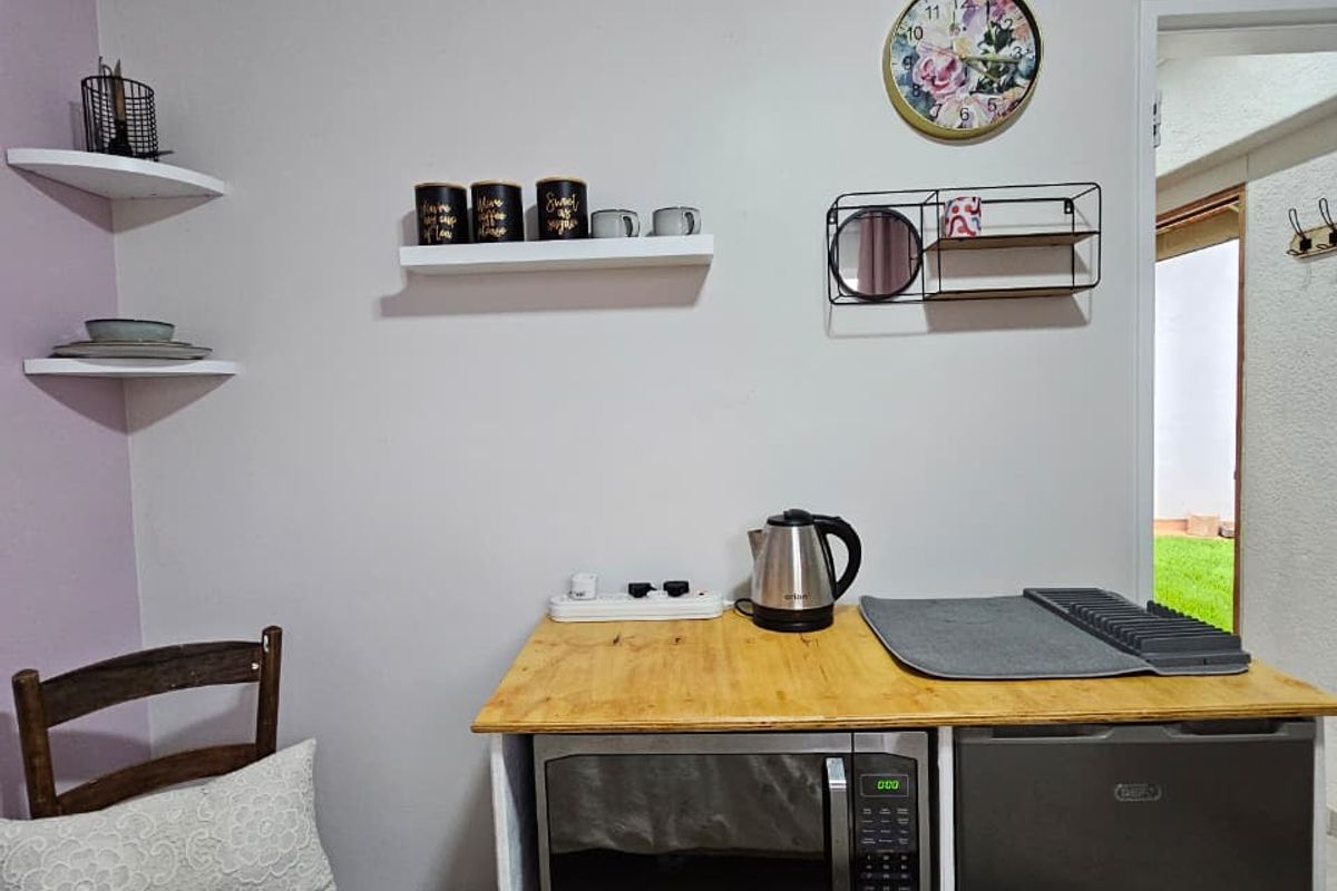 A compact kitchenette area featuring a built-in microwave, mini fridge, and floating wall shelving, suitable for a small studio or utility space.