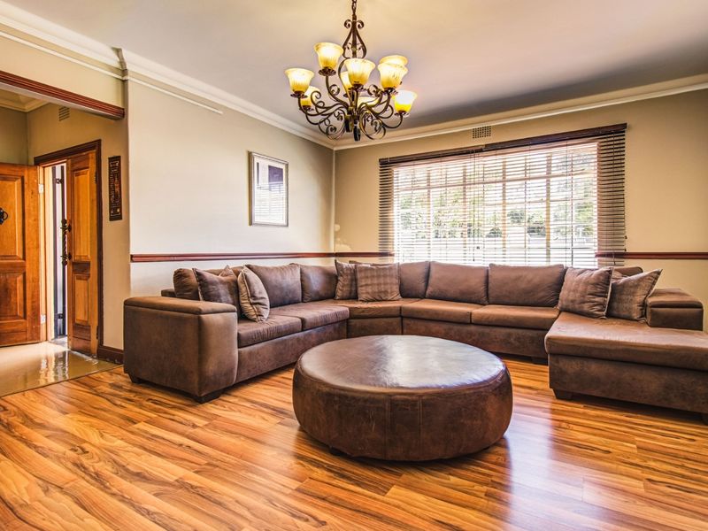 Spacious living room featuring warm laminate flooring, crown molding, and a classic chandelier, offering a comfortable and inviting atmosphere.