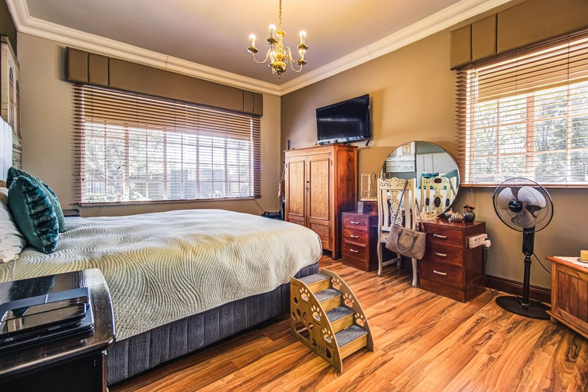 A well-lit bedroom featuring laminate flooring, crown molding, and dual windows with venetian blinds.