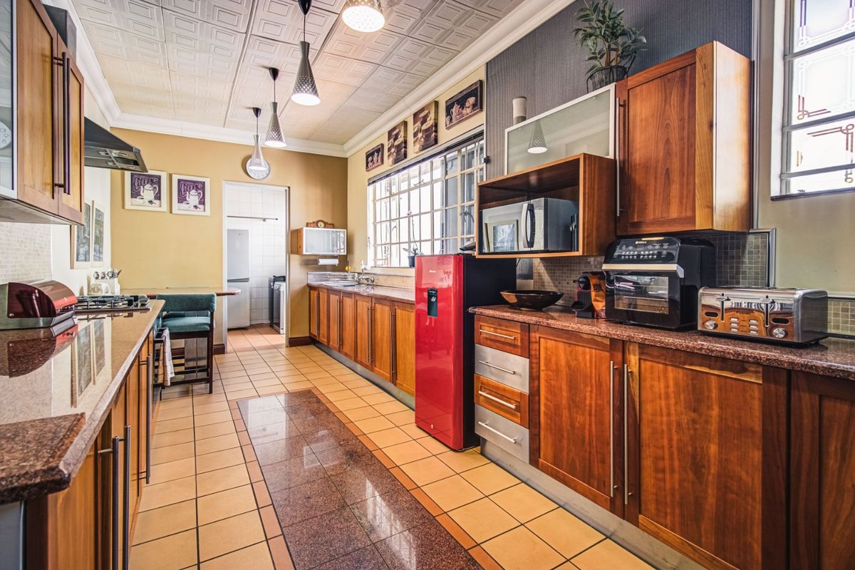 A spacious kitchen featuring warm wooden cabinetry, granite countertops, a gas hob, and a distinctive coffered ceiling, with an adjacent scullery area.