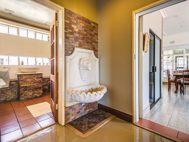 A transitional hallway area featuring a decorative wall-mounted stone fountain, brick accent wall, and tiled flooring, providing access to adjacent living and bathroom spaces.
