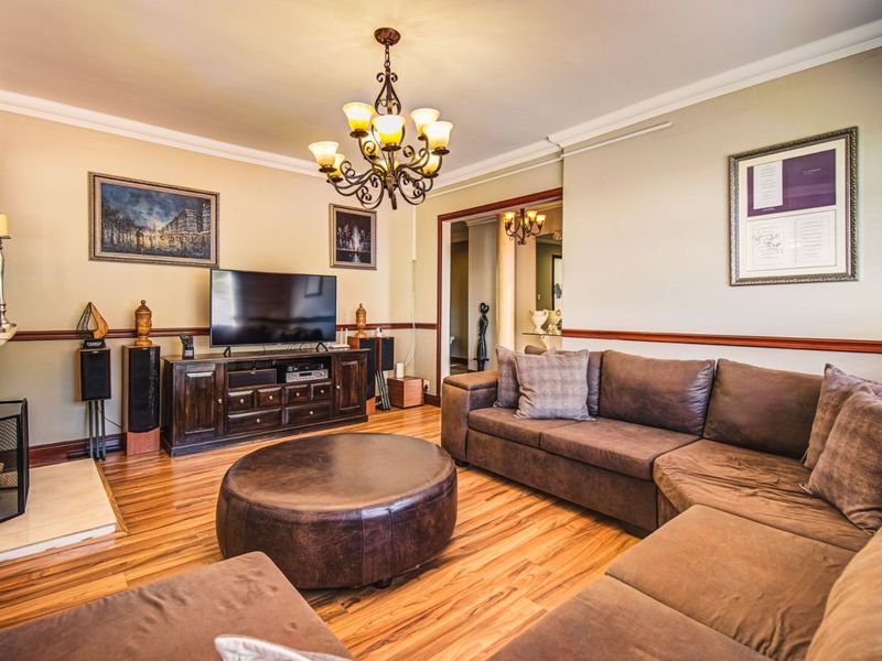 A well-maintained living room featuring hardwood flooring, crown molding, a chair rail, and a classic fireplace with a mantelpiece.